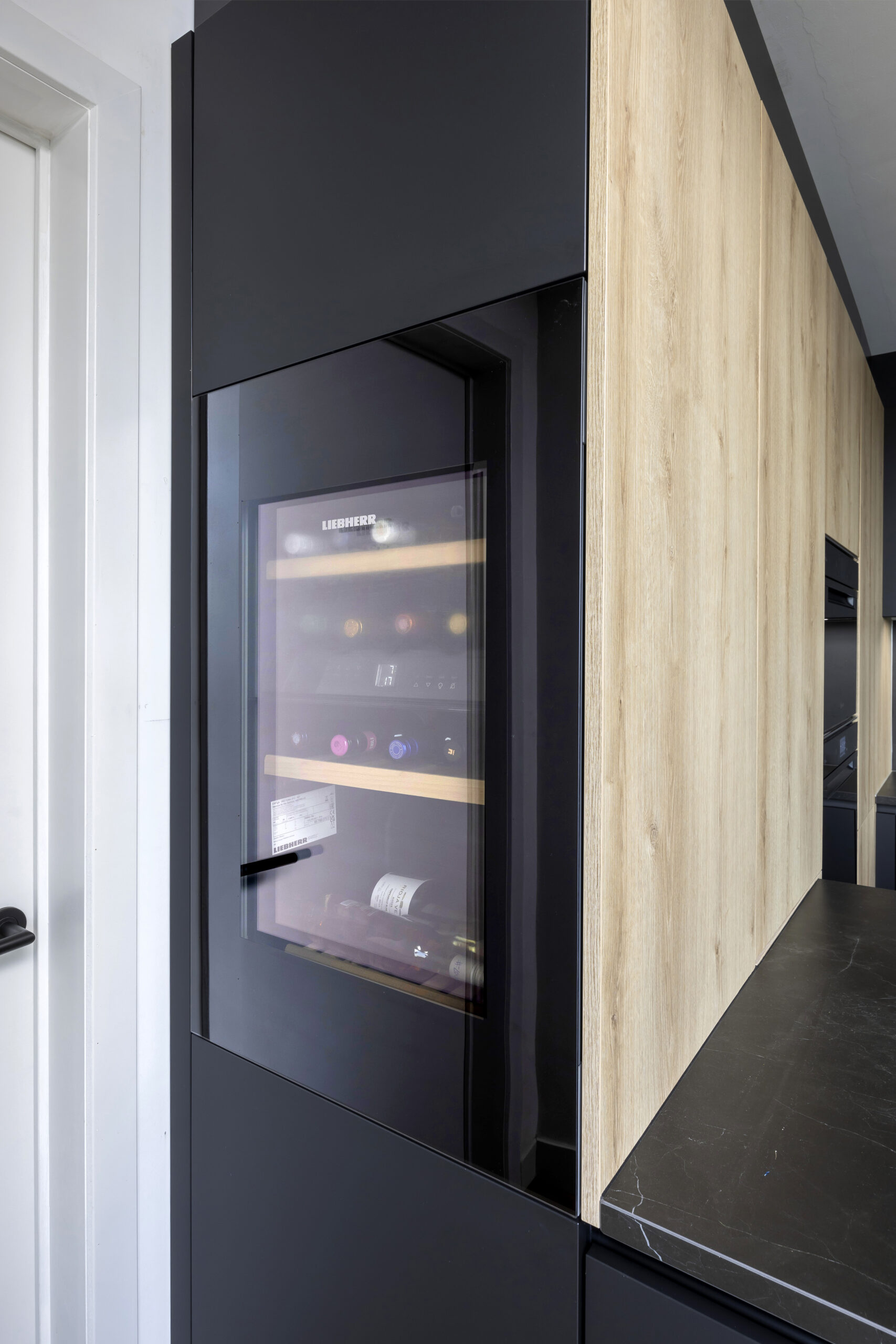 strakke zwarte moderne keuken met houttoets novy dampkap greeploos wijnkoeler liebher keramisch werkblad